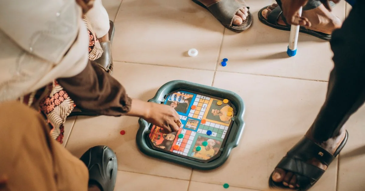 Groupe d'enfants jouant à un jeu de société à l'intérieur sur un sol carrelé, concentrés sur les pièces du jeu.