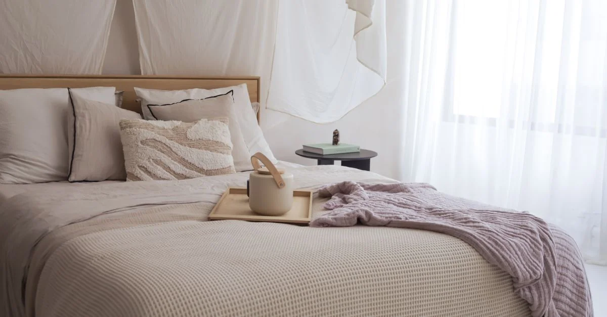 Une chambre à coucher élégante avec des textiles neutres, un éclairage doux et une théière sur un plateau pour une atmosphère cozy.