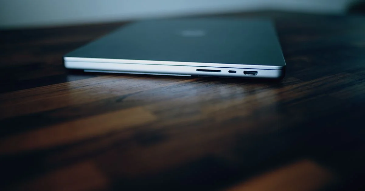 Vue latérale d'un ordinateur portable fermé montrant ses ports sur une surface en bois élégante.