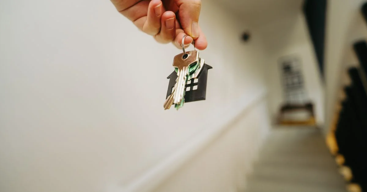 Gros plan d'une main tenant un porte-clés en forme de maison, symbolisant l'immobilier et la propriété.