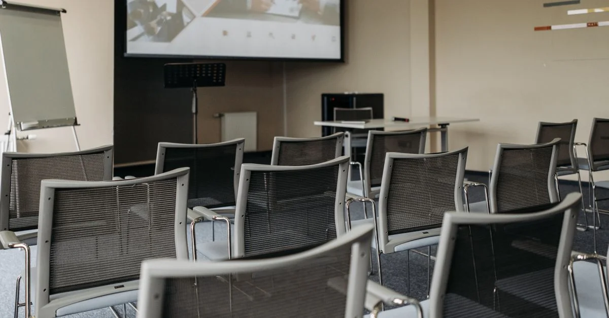 Configuration moderne d'une salle de conférence avec des chaises vides, un écran de projection et du matériel de présentation.