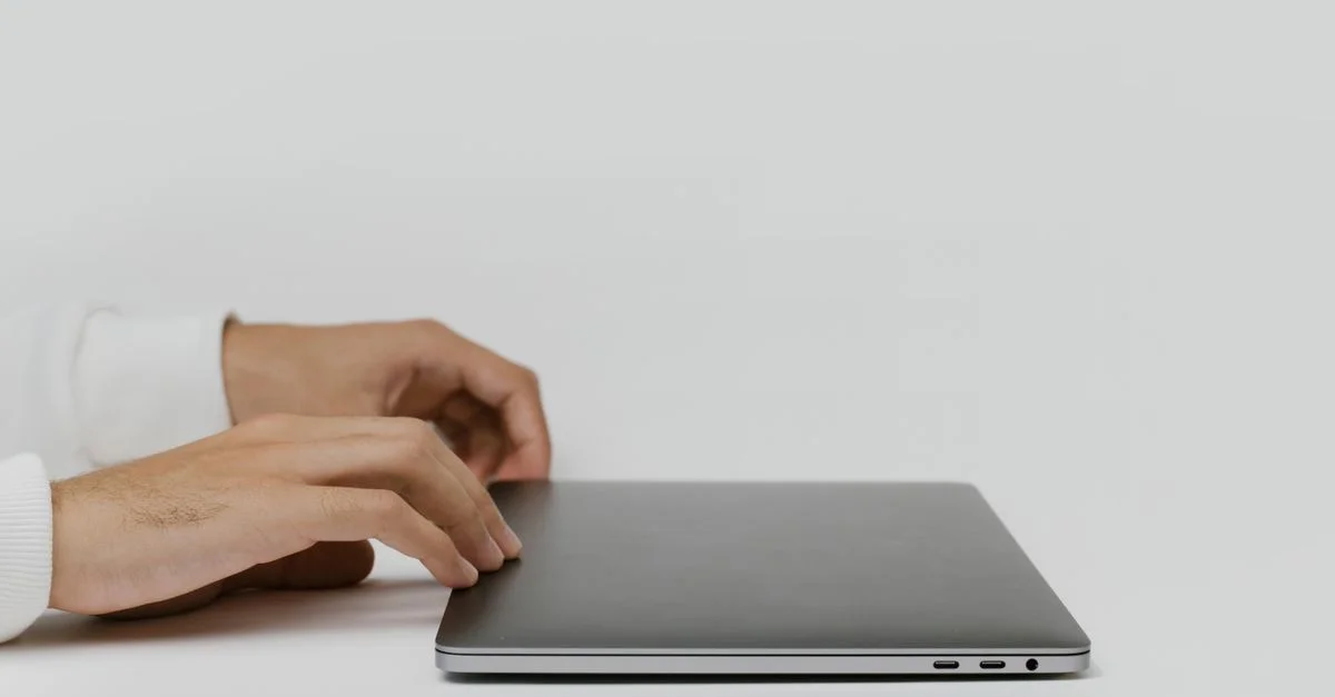 Mains préparant à ouvrir un ordinateur portable fermé sur un bureau minimaliste, prêtes à travailler.